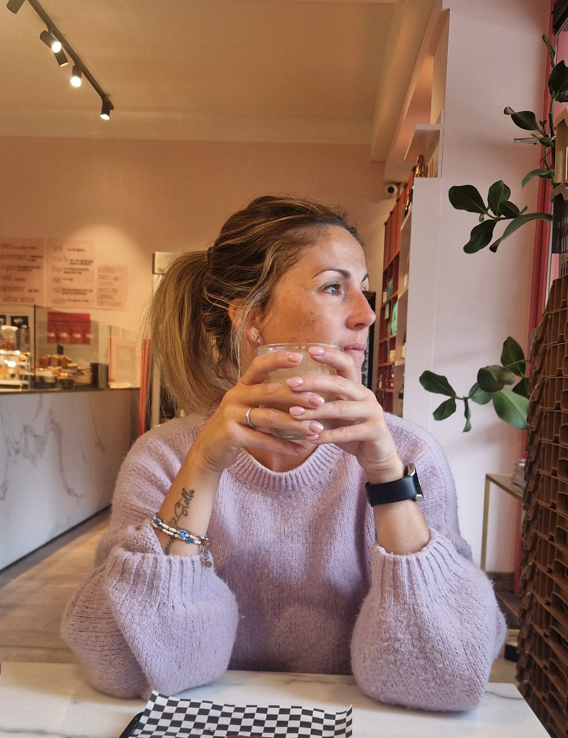 Vrouw in lila trui aan tafel in een koffiezaak